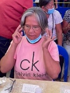 A Philippine woman is seen trying on a pair of glasses. She wears a pink shirt and is seen adjusting the glasses on her face. 